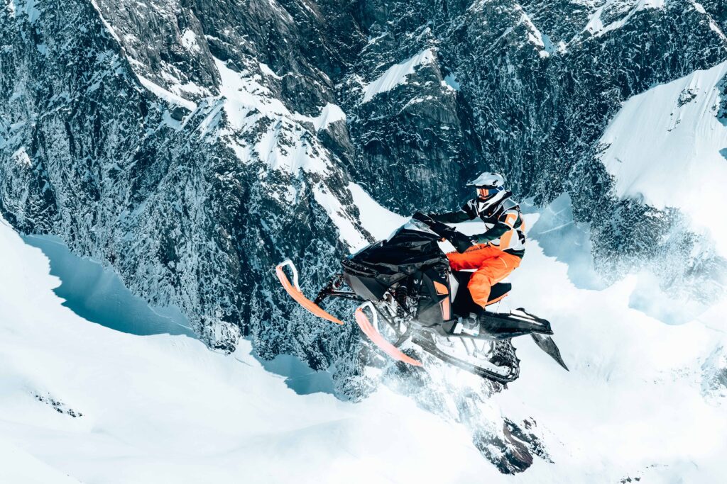 Snowmobile and rider making jump in winter landscape with mountains