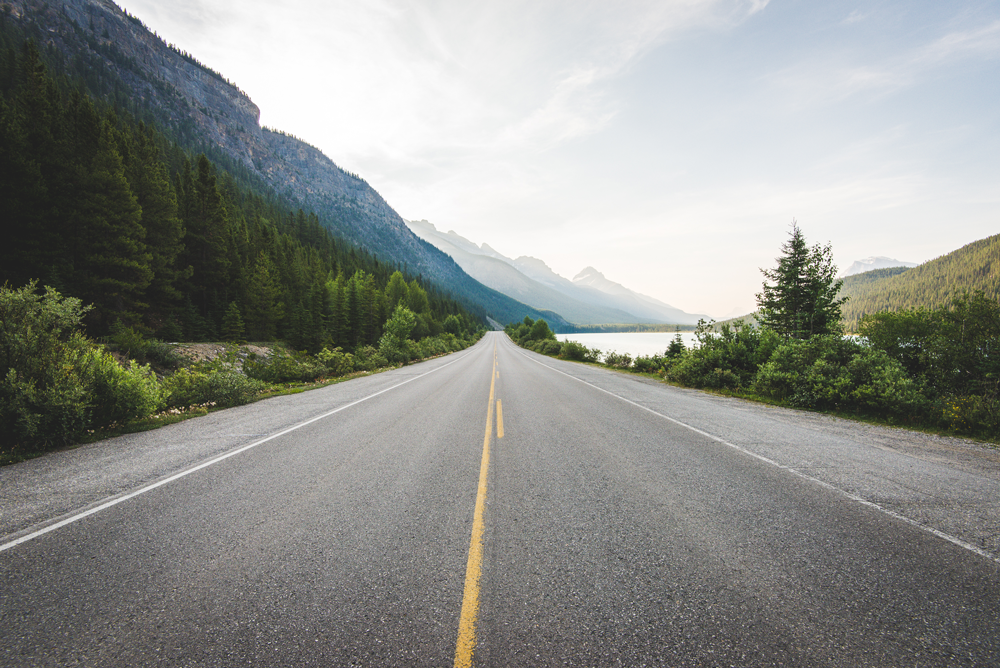 Asphalt road with yellow lines in wilderness with mountains and greenery with perspective looking forward